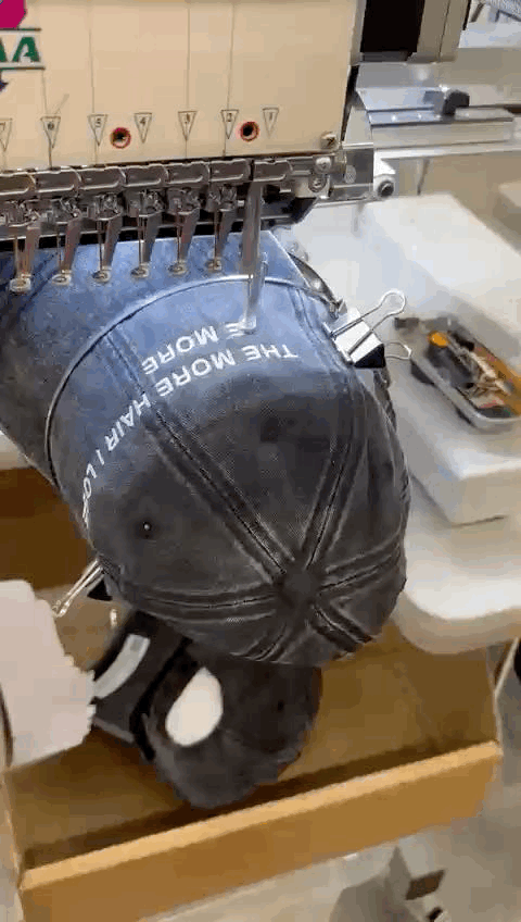 Embroidery machine stitching the custom design 'The More Hair I Lose The More Head I Get' on a cap