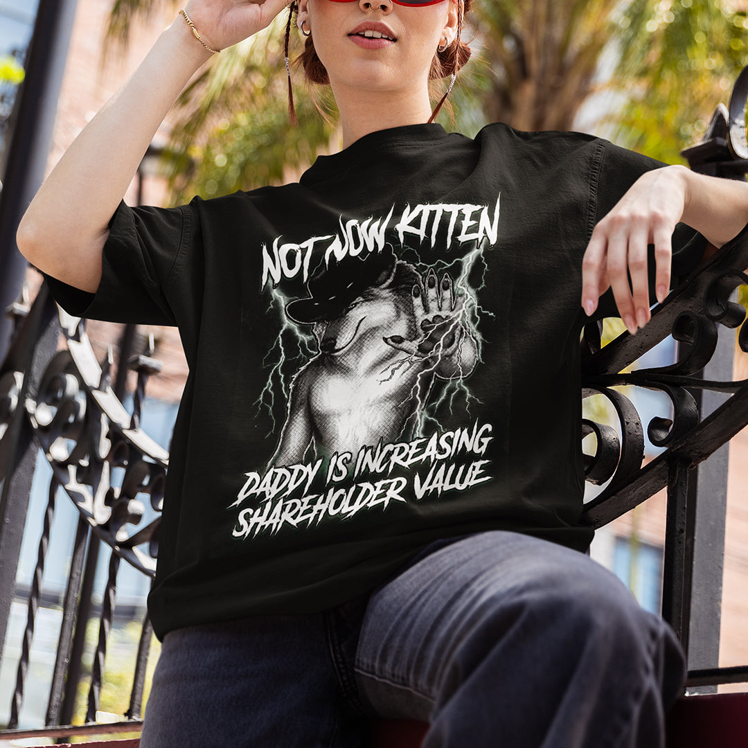 Person wearing a black t-shirt with graphic design and text, sitting outdoors.