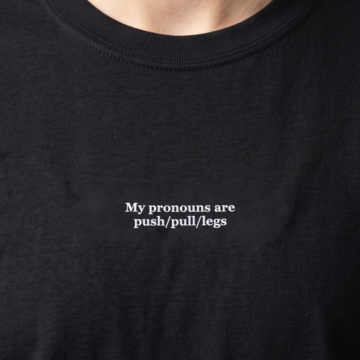 My pronouns are push/pull/legs (embroidered) T-Shirt in black, worn, close-up of the stitching