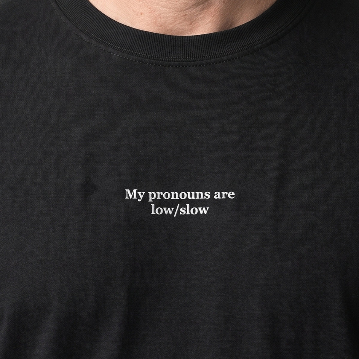 My pronouns are low/slow (embroidered) T-Shirt in black, worn, close-up of the stitching