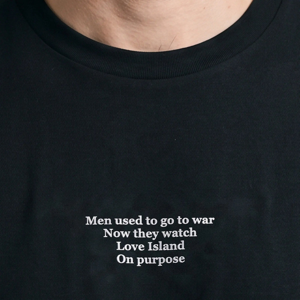 Men used to go to war now they watch Love Island on purpose embroidered t-shirt in black, worn, close-up of the stitching
